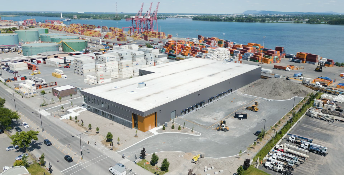 An ariel image of a newly constructed industrial building a 6100 Rue Notre-Dame Est. Montreal, Quebec, with an orange entrance, along the port and shipping yard.