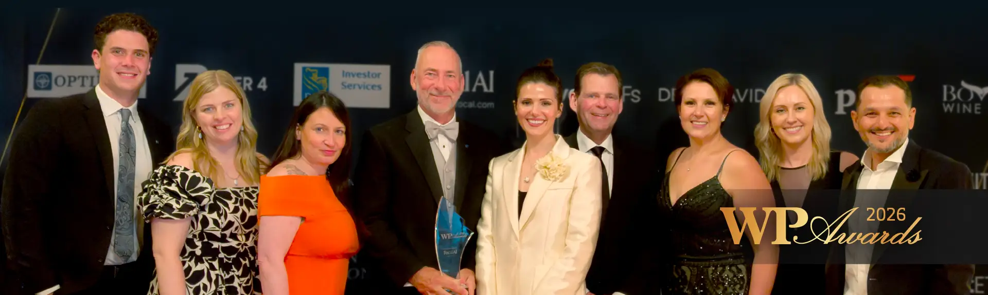 A group of smiling people posing with an award plaque at an awards event.